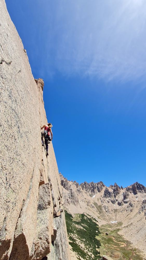 Luiza escalando uma parede de granito sob céu azul